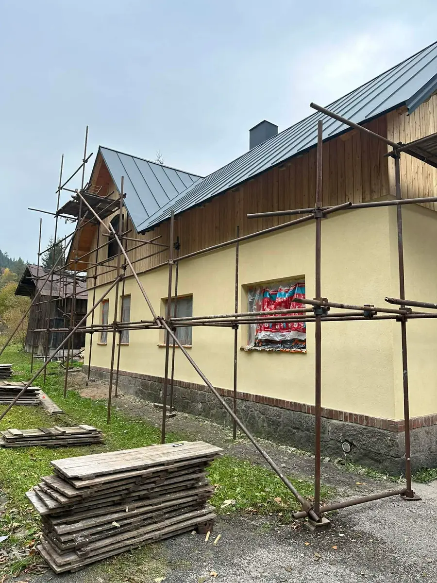 Zateplená fasáda domu na lešení, žlutá omítka a dřevěný obklad štítu